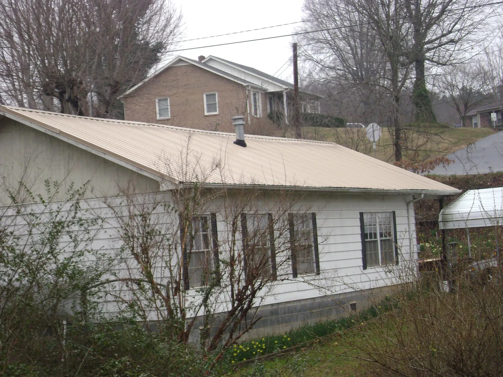 Tan metal roof on a white sided house set into a hillside — Commercial Roofing by Roofing Brothers in Vernon